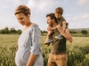 Familie spaziert über ein Feld, Mutter ist schwanger, Vater hat Kind auf den Schultern