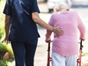 Seniorin geht an einem Rollator, Pflegefachkraft stützt sie 