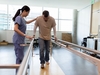 Patient in der Rehabilitation übt zu gehen und wird dabei von einer Pflegefachfrau betreut