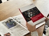 Person hält Studie in der Hand, Zeitungsartikel liegt auf dem Tisch