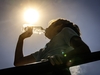 Ein Kind steht in der prallen Sonne und trinkt aus einer Wasserflasche