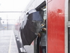 Roter Zug am Bahnhof, es regnet, Person steigt mit einem Regenschirm ein