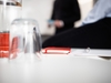 Rotes Notizbuch und Gläser, im Hintergrund sprechende Menschen