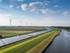 Auf der rechten Seite ein Fluss, daneben eine Solarkraftanlage, dahinter Windkraftanlagen 
