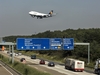 Eine befahrene Autobahn, darüber fliegt ein Flugzeug der Lufthansa