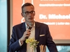 Michael Böhmer mit Mikrofon vor einer Leinwand, auf der ein Vortrag zu sehen ist