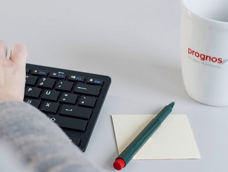 Eine Person tippt auf der Tastatur, neben ihr liegen ein Notizbuch und ein Stift